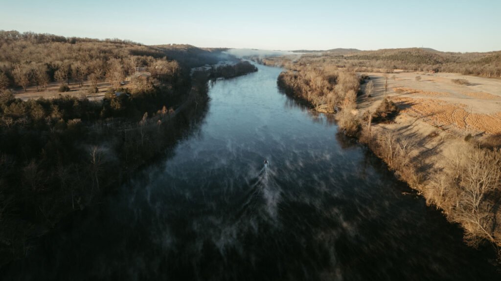 Aerial view of the White River in the early morning, with mist rising off the water and a single boat heading upstream between wooded banks.